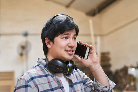 Craftsman as a carpenter trainee calls with the smartphone in the workshop