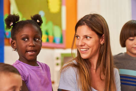 Childminder or kindergarten teacher and African girl in kindergarten or after-school care center