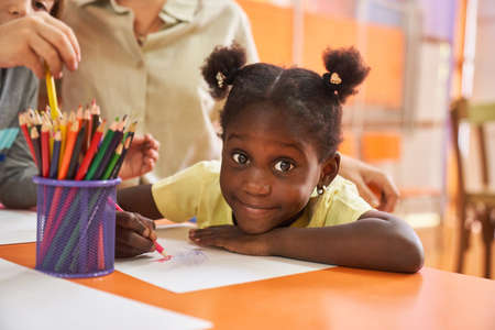African girl paints a picture with crayons on paper in international kindergarten