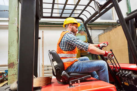 Warehouse worker as a forklift driver while driving a forklift in the warehouse of the factoryの写真素材