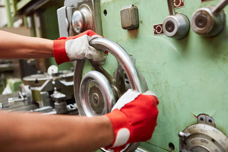 Metalworker turns the big wheel of a drill press in a metalworking factory