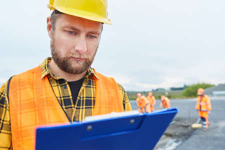 Construction worker with checklist controls construction progress on construction site in road...