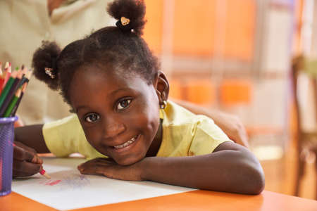 Happy girl with pigtails paints a colorful picture with crayons in the elementary school painting classの写真素材