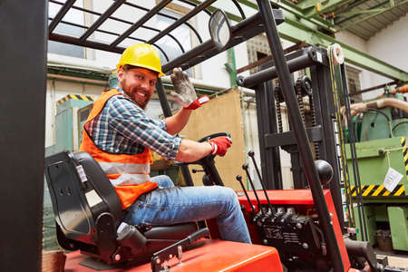 Waving forklift driver in the warehouse of a haulage company while driving forklift