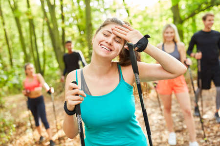Exhausted young woman on Nordic walking course with friends in nature in summer