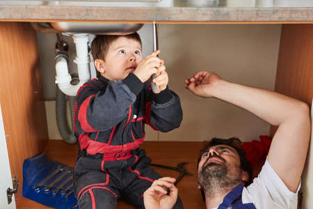 Handyman child helps his father install or repair a sink