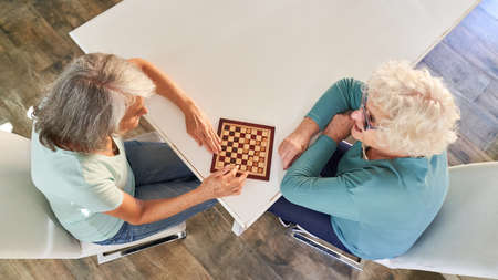 Two retired senior women playing checkers as a leisure activity at homeの写真素材