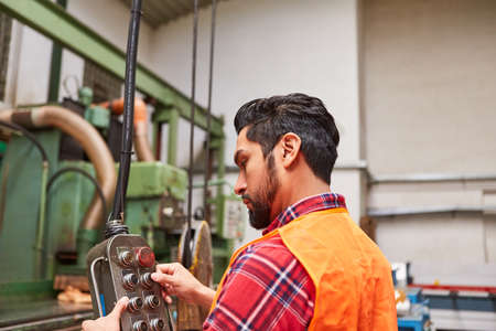 Young man as a worker at the control panel of a coordinate drilling machine or crane