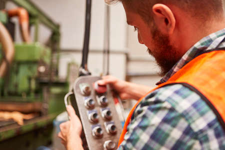 Worker as a machinist in the factory operates the buttons on the control of a machine