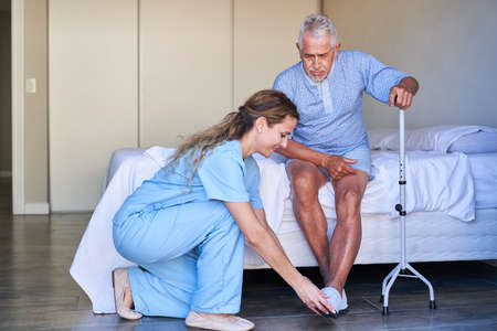 Geriatric nurse helps senior with walking aid to put on shoes in a nursing home or hospital