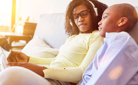 African mother and son at home on sofa using laptop computer while video chat