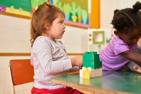 Girls in international kindergarten or preschool plays with building blocks at the tableの写真素材
