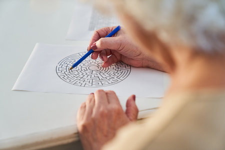 Elderly woman with pen solves a maze puzzle as a brain teaser and memory training against dementiaの写真素材