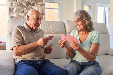 Elderly retired couple playing cards on the sofa at home in the apartment