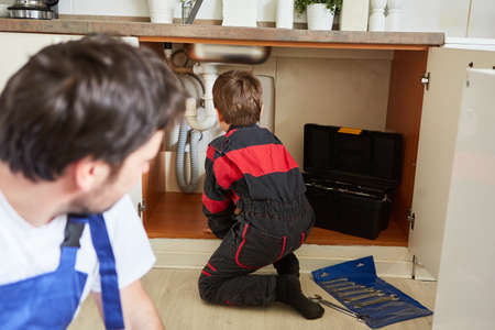 Son helps father as a do-it-yourselfer repairing or installing the sink in the kitchen