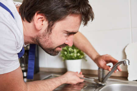 Handyman repairs defective faucet on the tap on the sink in the kitchenの写真素材