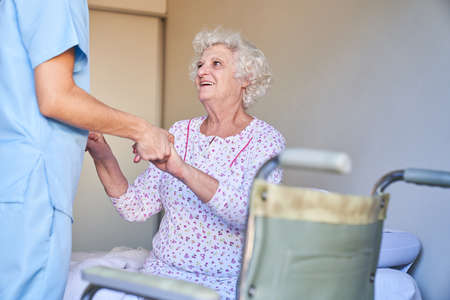 Caregiver helps senior citizens with dementia to get up in the nursing home or retirement homeの写真素材