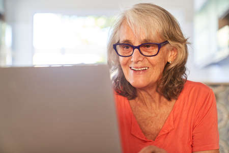 Smiling elderly woman video chatting or typing email on laptop computer at home