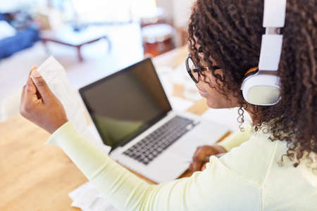 African woman at computer with receipt on tax return or checking finances at home