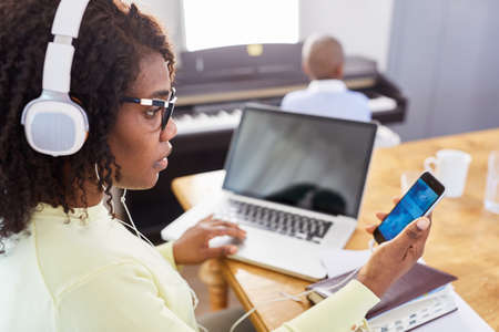 African woman with headset having a video chat in the home office with child at the piano in the backgroundの写真素材