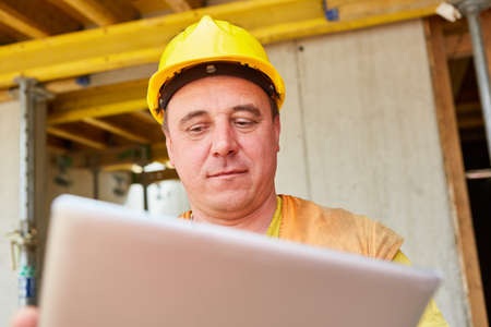 Construction worker as a foreman looks at tablet computer during house construction planning on the...