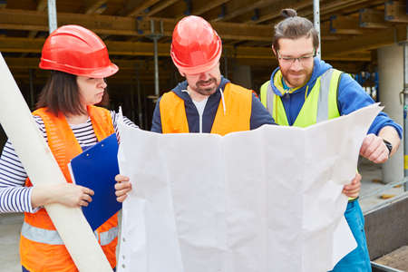 Architect and craftsman team with construction drawing on a new construction site during...
