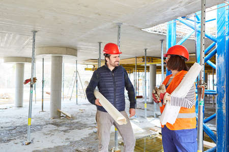 Architect with blueprint and workers plan construction work or renovation on the construction site...