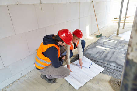 Craftsmen and architect with a blueprint in the shell of the construction site discuss the...