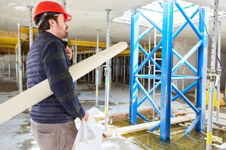 Architect with hard hat and building drawing in the shell of the construction site of the house...