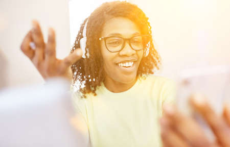 African woman with headphones video chat on smartphone in home office