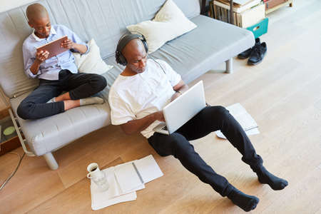 Man in the home office on laptop during a video conference and boy with tablet PC on the sofa