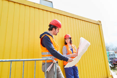 The architect and craftsman as foreman look together at a building plan for the house