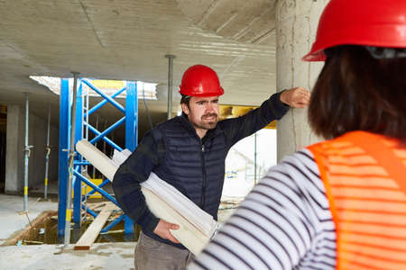 Craftsman and architect with construction drawing together in the shell construction during...