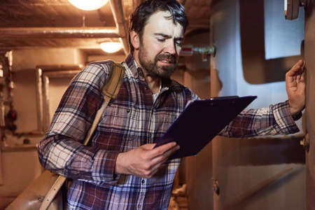 Heating installer checks condensing boiler of a gas heating system in the basement with a checklistの写真素材