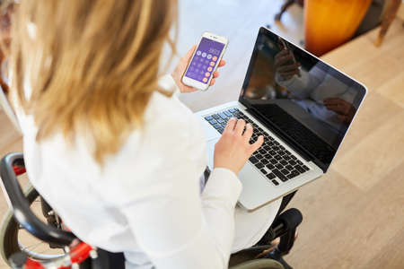 Woman in a wheelchair using laptop computer and calculator while banking online in the home office