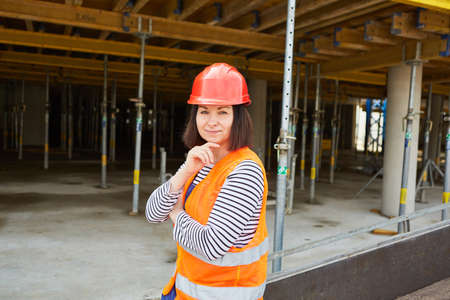 Woman as a construction worker with a hard hat or architect in front of the shell of a building site...