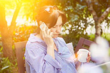 Woman talking on the phone on smartphone in the garden hangs on hold while waitingの写真素材