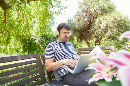 Freelancer on vacation in the green garden at the laptop computer during a video conferenceの写真素材