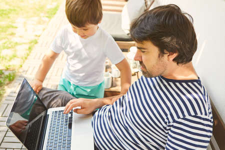 Freelancer as a father on the laptop computer together with his son at homeの写真素材