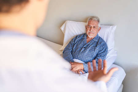 Senior patient in bed in hospital lists to his doctor during rounds as a consultation