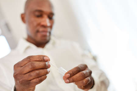 African man doing self-test with saliva sample as protection and control at homeの写真素材