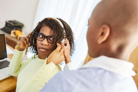 Son disturbs his mother with headset on the computer during an online video conference in the home officeの写真素材