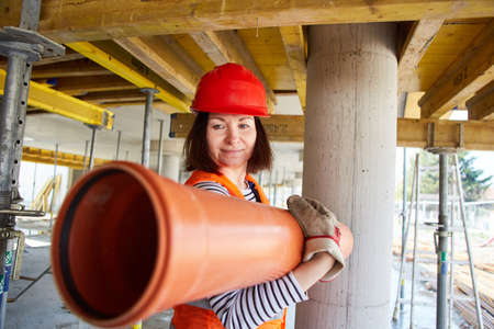 Woman as a craftsman or construction worker carries a plastic water pipe in the shell of the...
