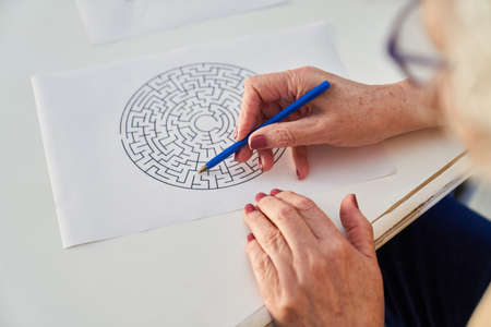 Elderly hands with pen solving maze puzzles as memory training against dementiaの写真素材