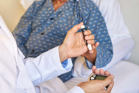 Doctor measures blood sugar on the finger of senior patient with a blood glucose meter in the retirement homeの写真素材