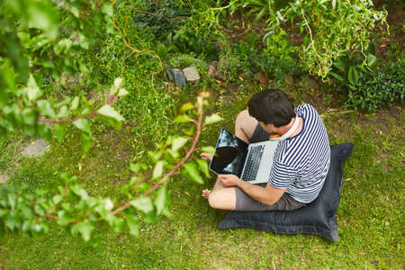 Man working on laptop computer in green garden in summer as freelancer programmer