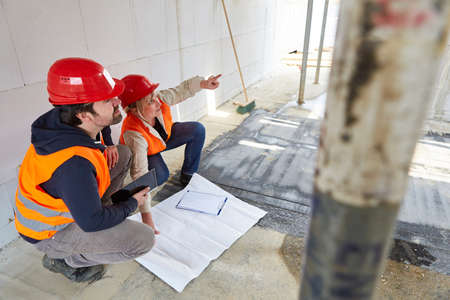 Architect team with floor plan on the construction site in the shell construction during the...