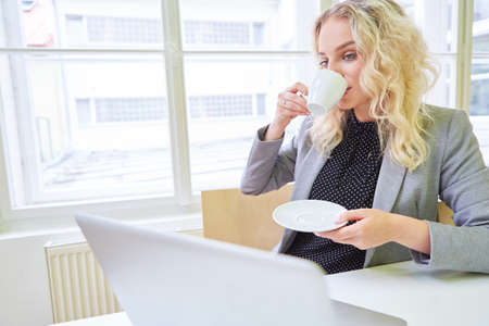 Young businesswoman at laptop computer drinking a cup of coffee during a breakの写真素材
