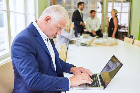 Mature businessman as manager or business consultant writes on laptop computerの写真素材
