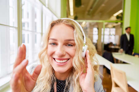 Cheerful young business woman with headphones waving during a video conference in the office